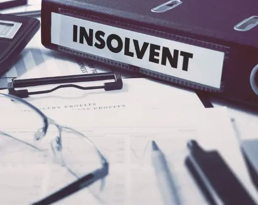 Půjčka po insolvenci-Šanon označený „INSOLVENT“ položený na finančních dokumentech s grafy, brýlemi a perem na stole, symbolizující stav úpadku a finanční problémy.